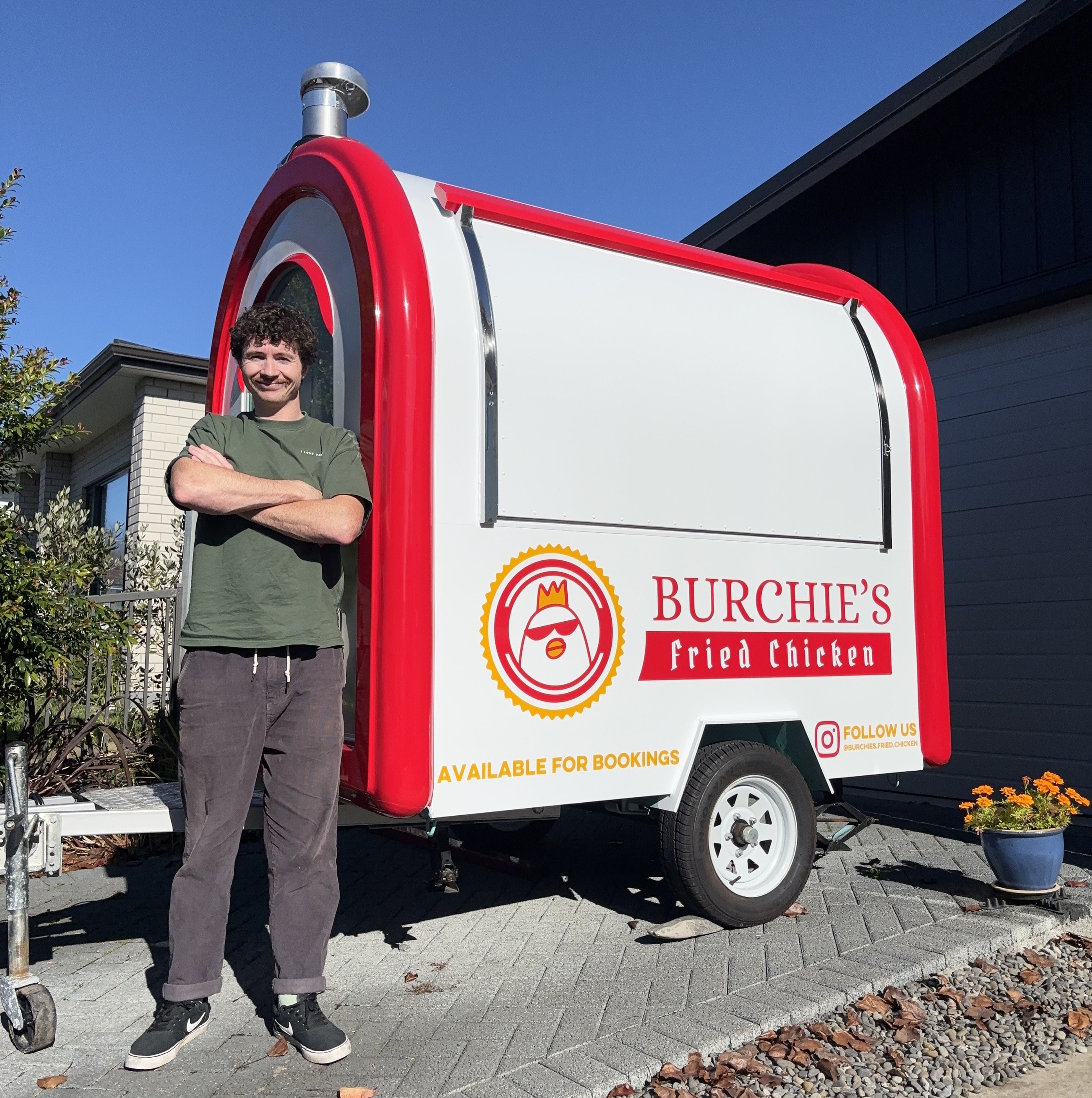 Burchie standing beside the red-and-white Burchie's Fried Chicken trailer